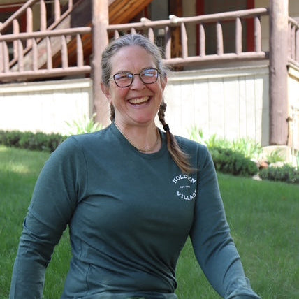 Woman sitting outdoors wearing a green long-sleeve shirt and green pants with a visible brand logo.