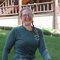 Woman sitting outdoors wearing a green long-sleeve shirt and green pants with a visible brand logo.