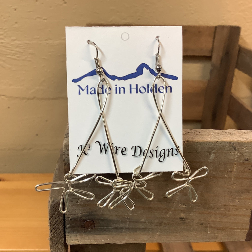 A pair of handmade silver wire dangle earrings displayed on a white backing card that reads 'Made in Holden' and 'K3 Wire Designs,' hanging on a rustic wooden shelf in an indoor setting. SKU 8088