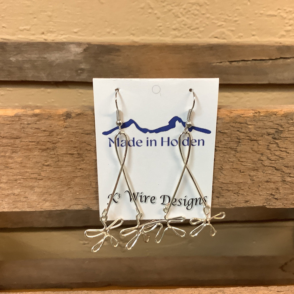 A pair of handmade silver wire dangle earrings displayed on a white backing card that reads 'Made in Holden' and 'K3 Wire Designs,' hanging on a rustic wooden shelf in an indoor setting. SKU 8089