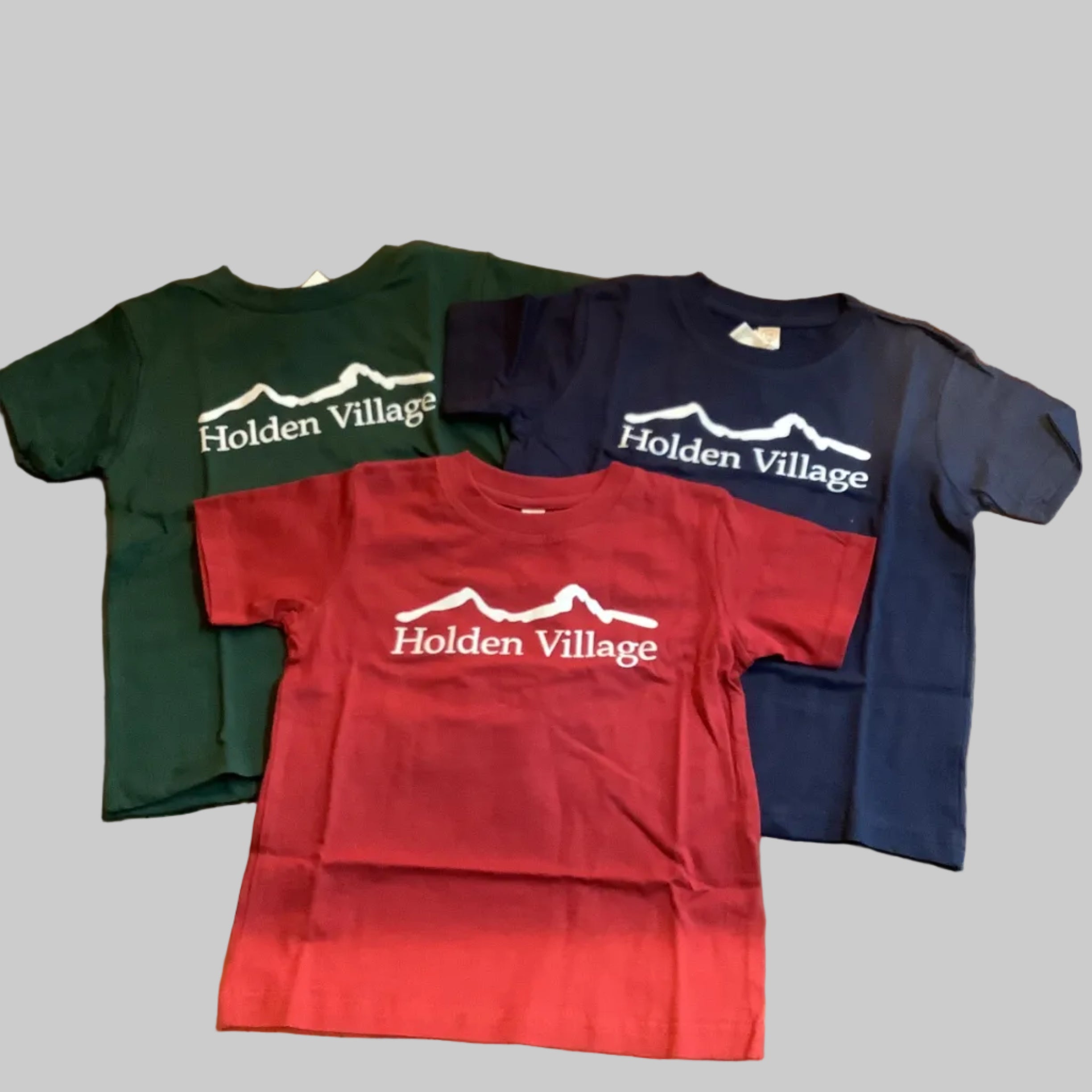 Three t-shirts in red, blue, and green  'Holden Village' logo branding.