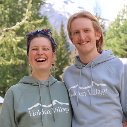 Two people wearing Holden Village hoodies with a mountainous background.