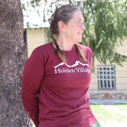 Person wearing a maroon shirt with 'Holden Village' logo, standing outdoors.