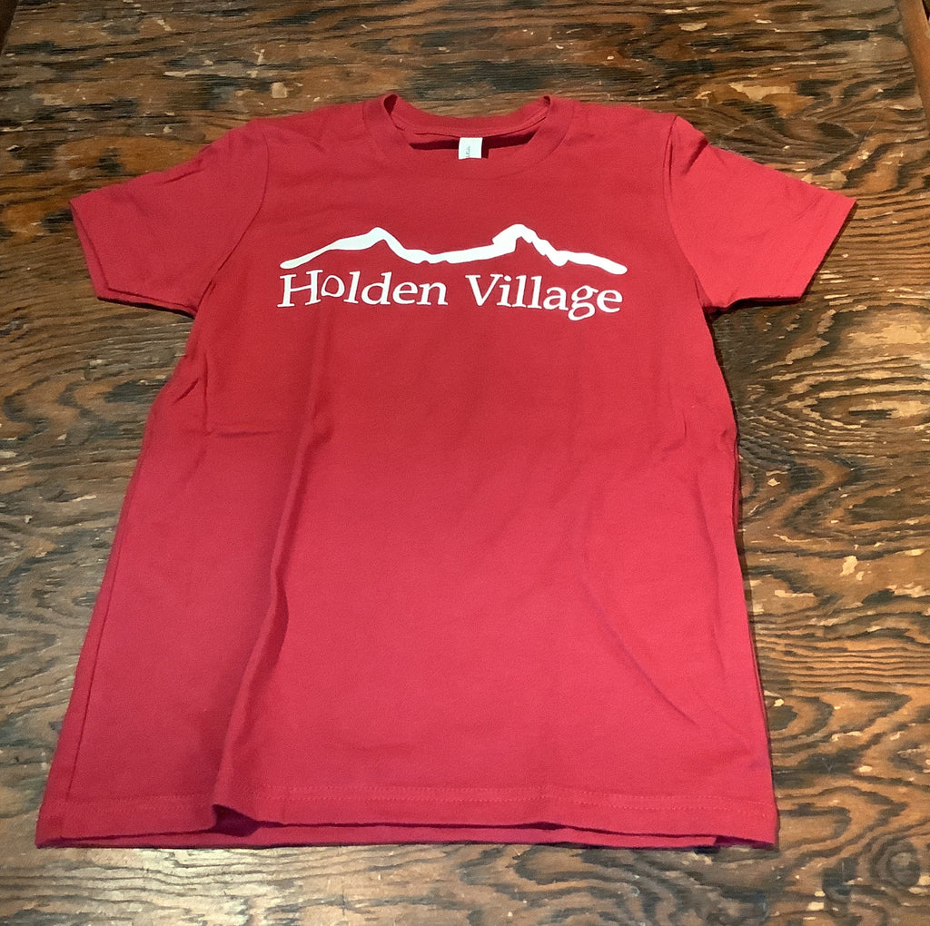 A folded red t-shirt with white text reading 'Haiden Village' and a white mountain graphic, laid flat on a dark wood surface.
