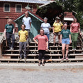 Group of people standing on wooden steps in front of a cabin-style building.