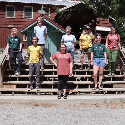 Group of people standing on wooden steps in front of a cabin-style building.