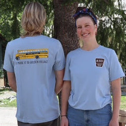 Two people standing outdoors near a tree, wearing matching light blue t-shirts.