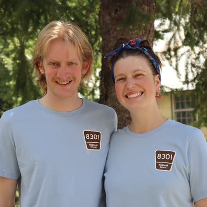 Two people wearing matching light blue t-shirts with a logo outdoors.