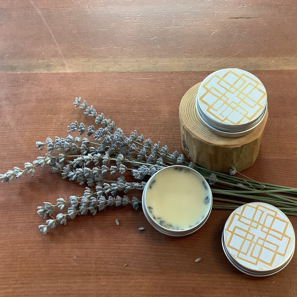Two jars of cream with decorative lids on a wooden surface with lavender sprigs.