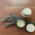 Two jars of cream with decorative lids on a wooden surface with lavender sprigs.