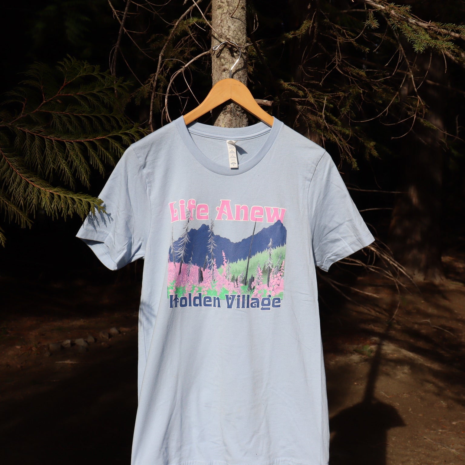 Light blue t-shirt with a graphic design hanging on a tree branch in a forest setting