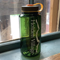 A translucent dark green Nalgene water bottle with 'Holden Village' printed vertically in white. Dark green top w yellow strap.