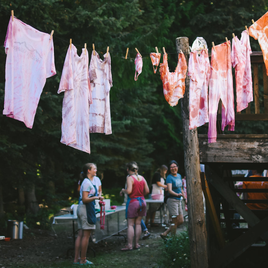Dyed fabrics hanging on a clothesline outdoors with people standing nearby.