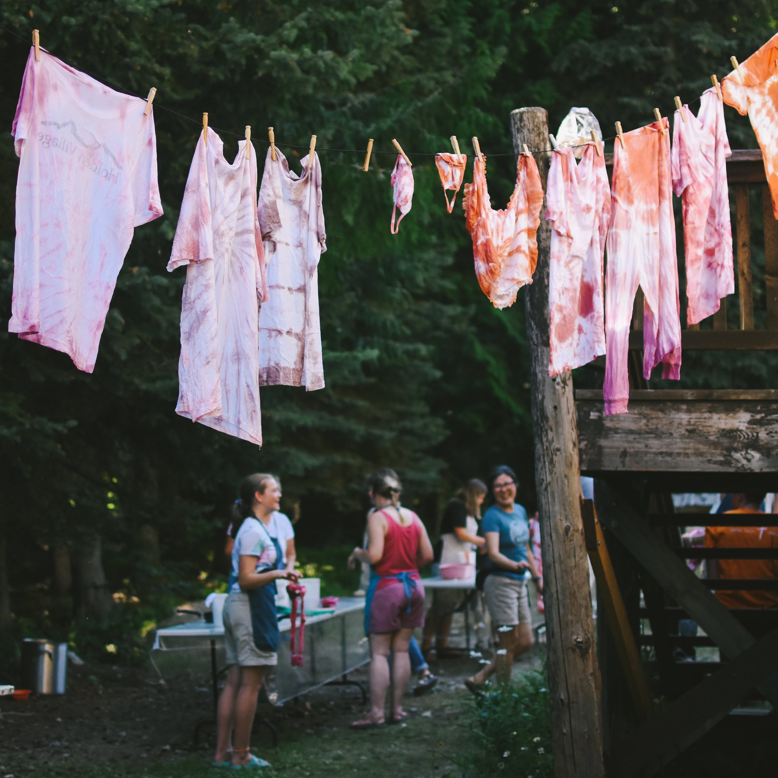 Dyed fabrics hanging on a clothesline outdoors with people standing nearby.